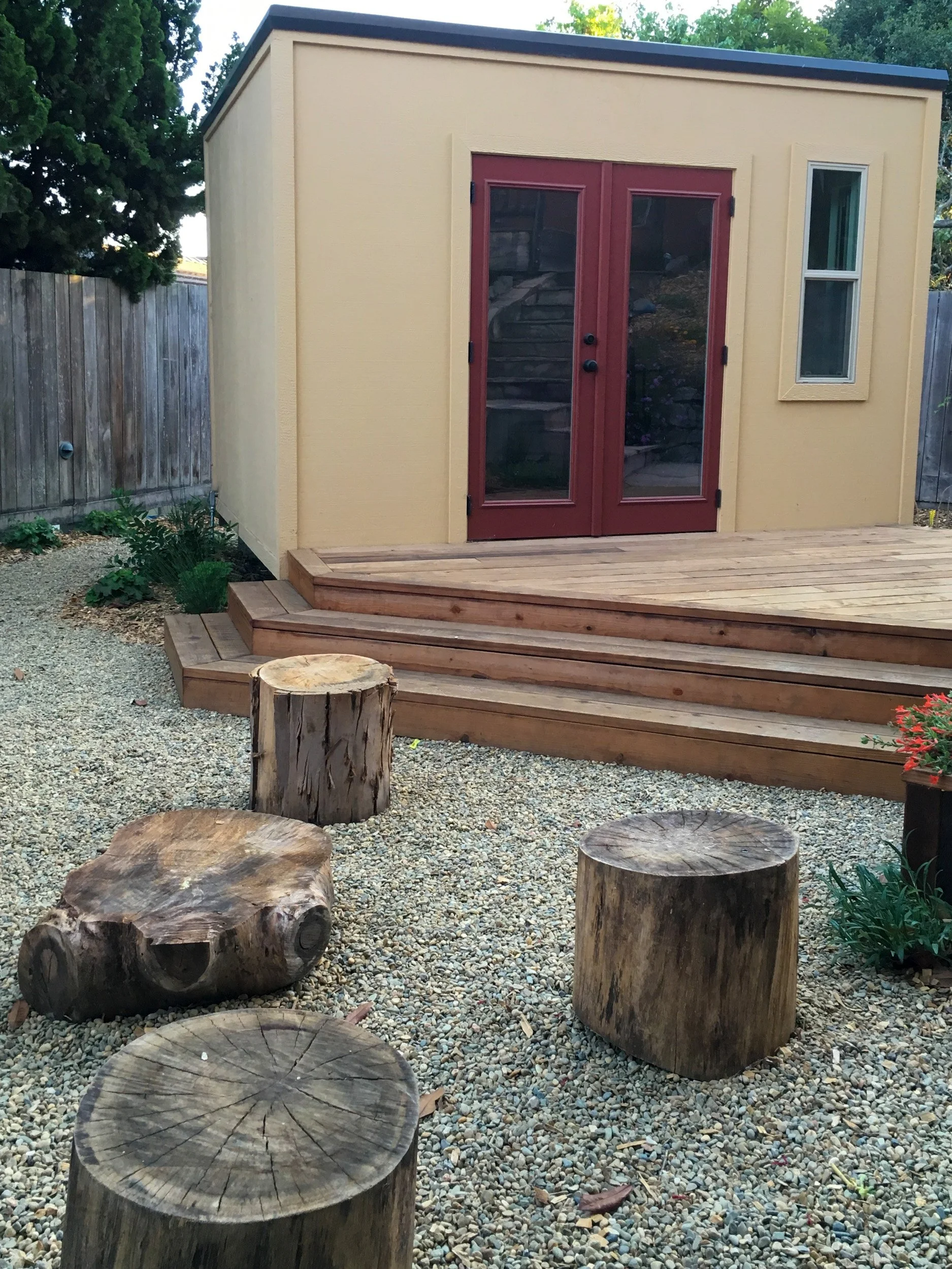 Wood deck with log seating in gravel patio in front of ADU