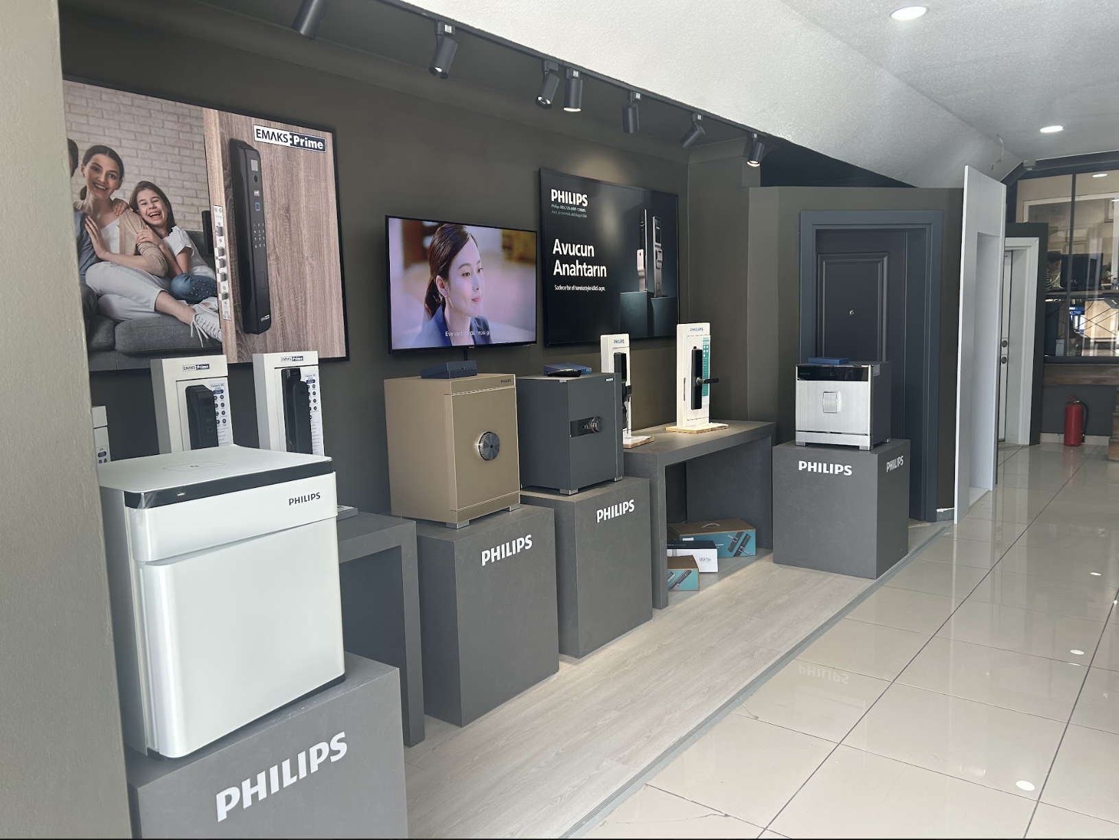 Duvara monte edilmiş ekranlar ve spot aydınlatma ile bir perakende mağazasında, kasalar ve uzaktan kumandalar da dahil olmak üzere çeşitli Philips ve EMaks Prime ev aletleri ve cihazlarının sergilenmesi.