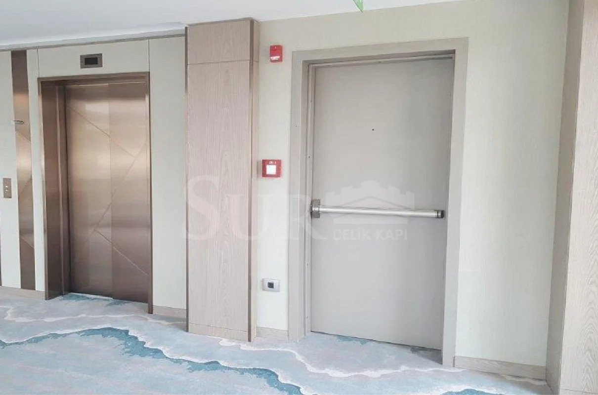 Açık renk duvarlara ve desenli halıya sahip bir binanın içinde bir asansör ve bir yangın kapısı.