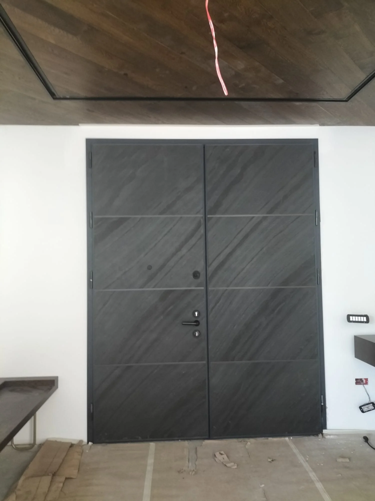 Black double door with horizontal panels in a room under construction.