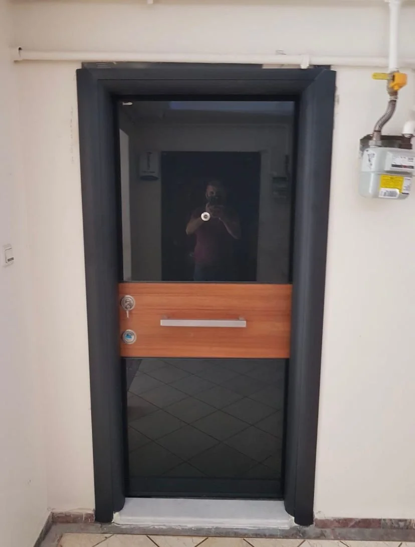 A black door with a window and a horizontal wooden panel in the middle, located in a white wall interior.