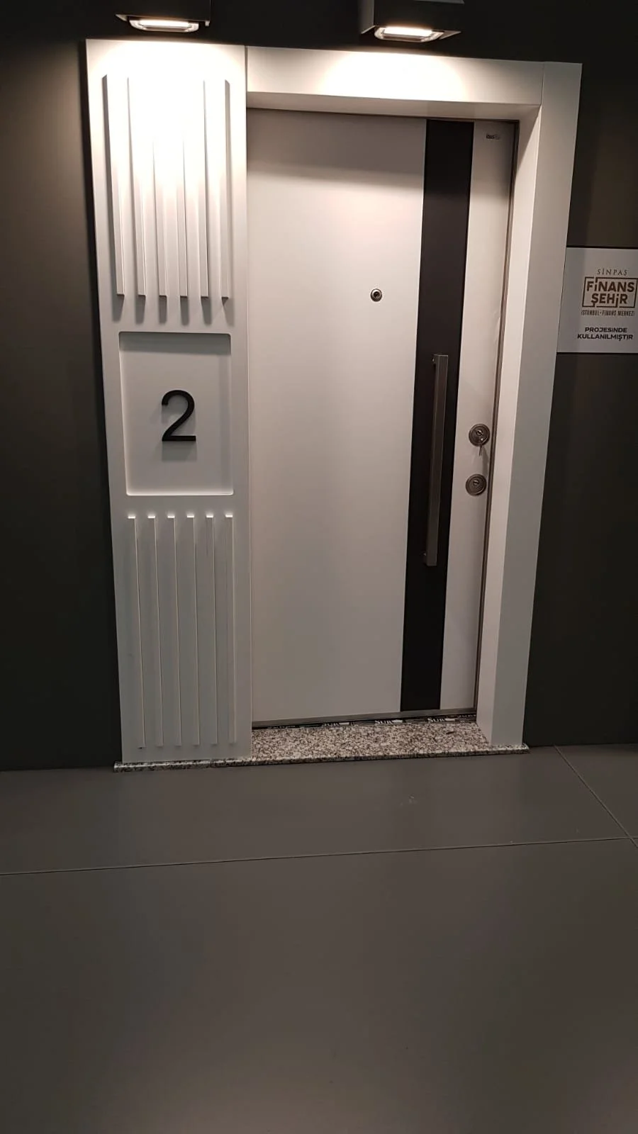 Modern elevator door with a black vertical accent, and a panel beside it with the number 2 and decorative white panels.
