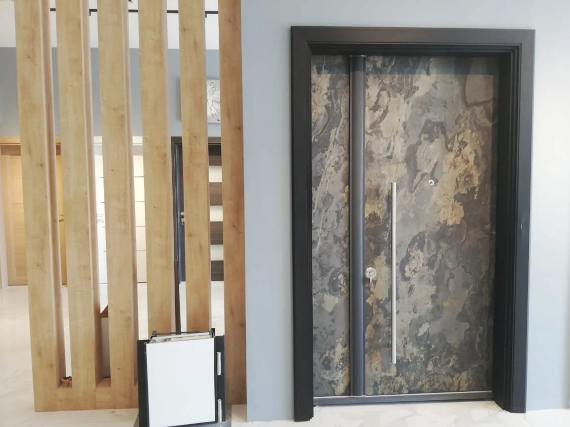 Decorative door with black frame and stone-like surface, with vertical metal handles, situated in a modern interior next to wooden slats.
