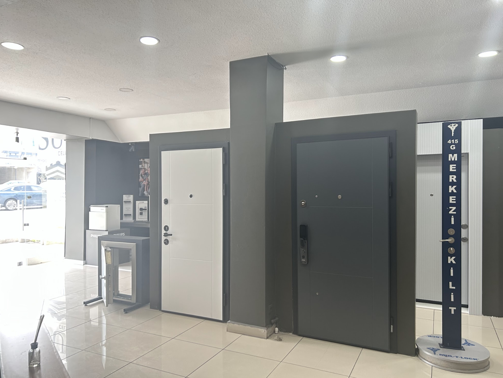 Güvenlik kapıları, güvenlik kilitleri sergisi ve vitrinin yanında bir ATM makinesi bulunan bir çilingir dükkanının iç görünümü.