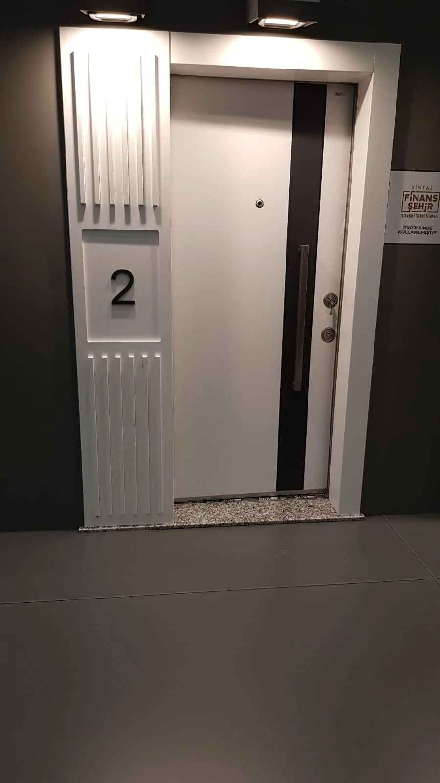 White elevator door with the number 2 displayed beside it, located in a modern building corridor.