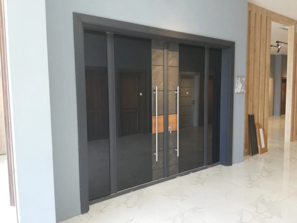 Glass sliding door with black frames and long vertical handles, leading into another room, with a wooden wall or panel to the right and beige marble flooring.