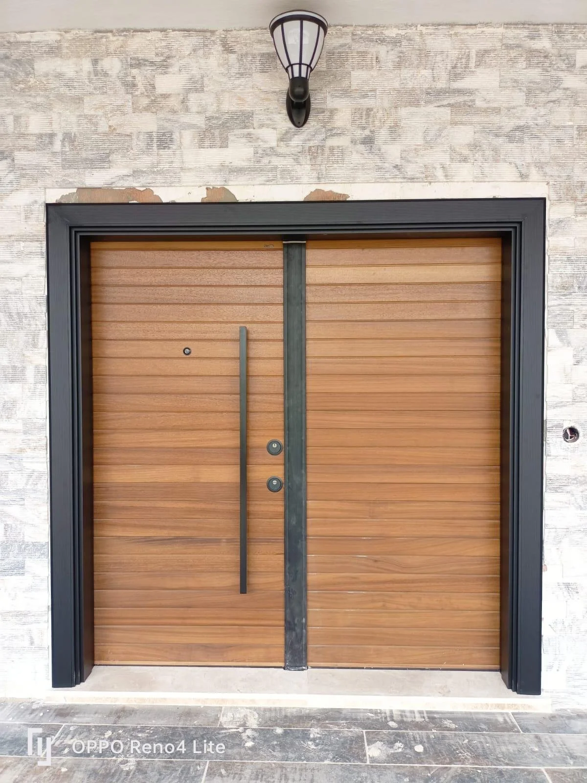 Double wooden garage doors with black frame, mounted on a textured exterior wall, illuminated by a black lantern-style light fixture.