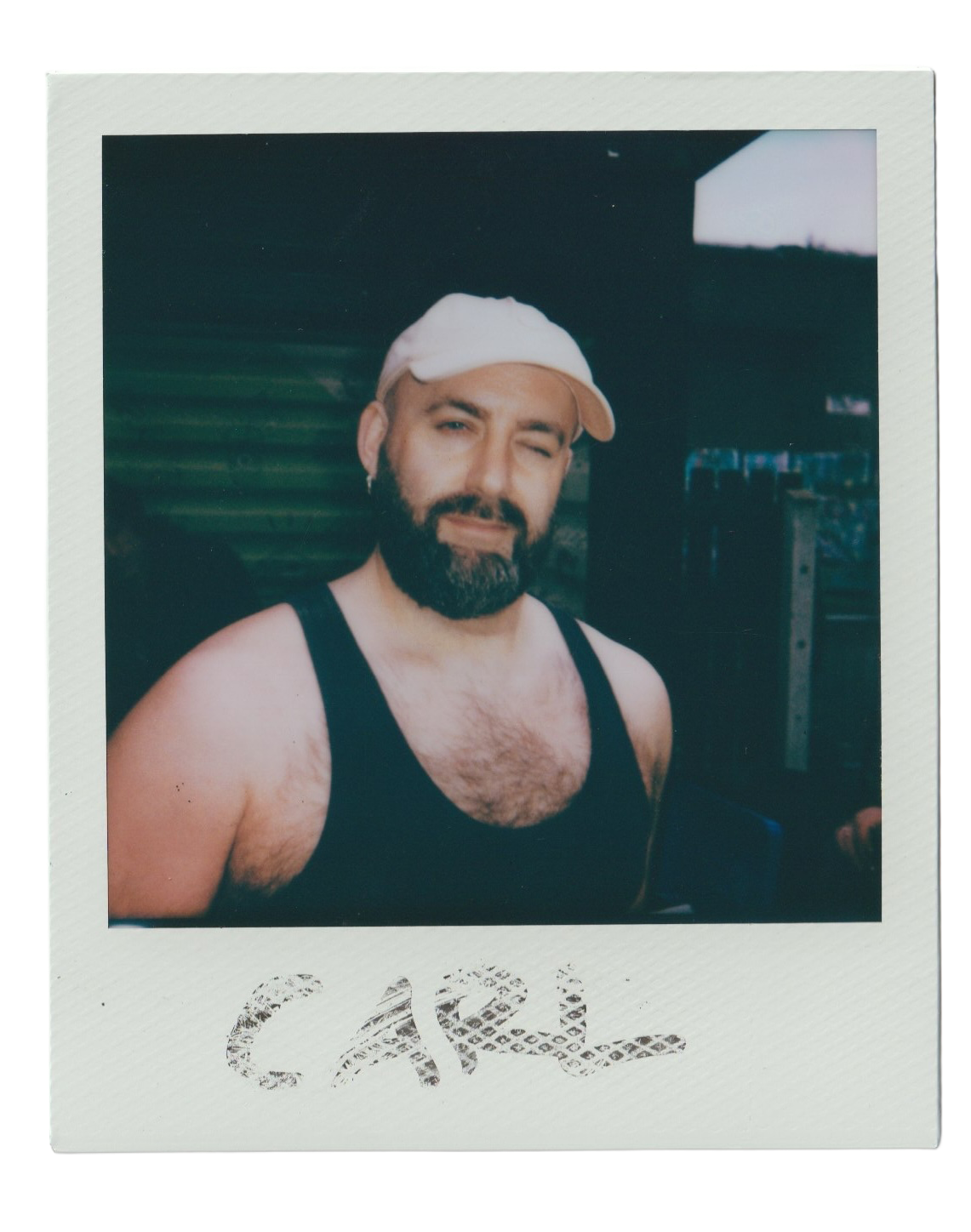 A man with a beard, wearing a white cap and black tank top, winking at the camera.