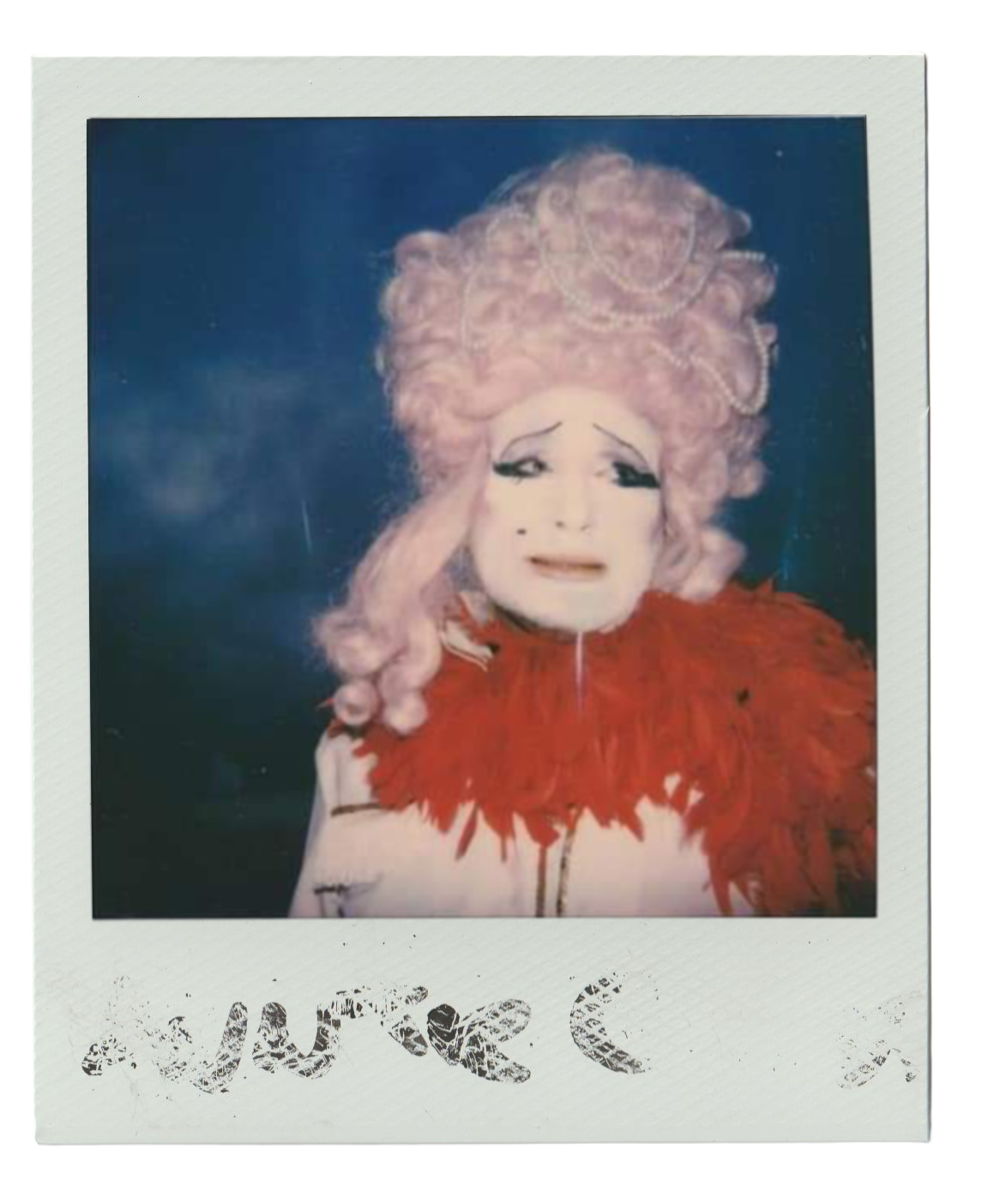A Polaroid photograph of a person wearing an elaborate costume with a pink wig, exaggerated makeup, and a red feathered collar, making a theatrical expression against a dark background.