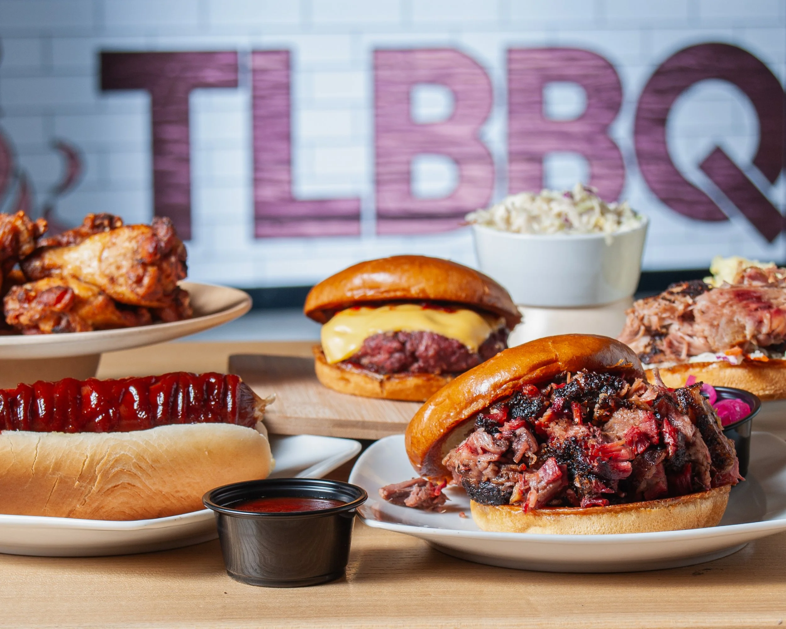 Popular food items pulled pork sandwiches, smoked cheeseburger, hot beef polish sausage, coleslaw, smoked chicken, and homemade barbecue sauce TLBBQ sign in the background.
