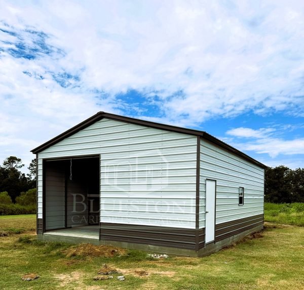 Large outdoor metal shed with one roll-up garage doors and a single side door in a grassy area surrounded by tall pine trees.