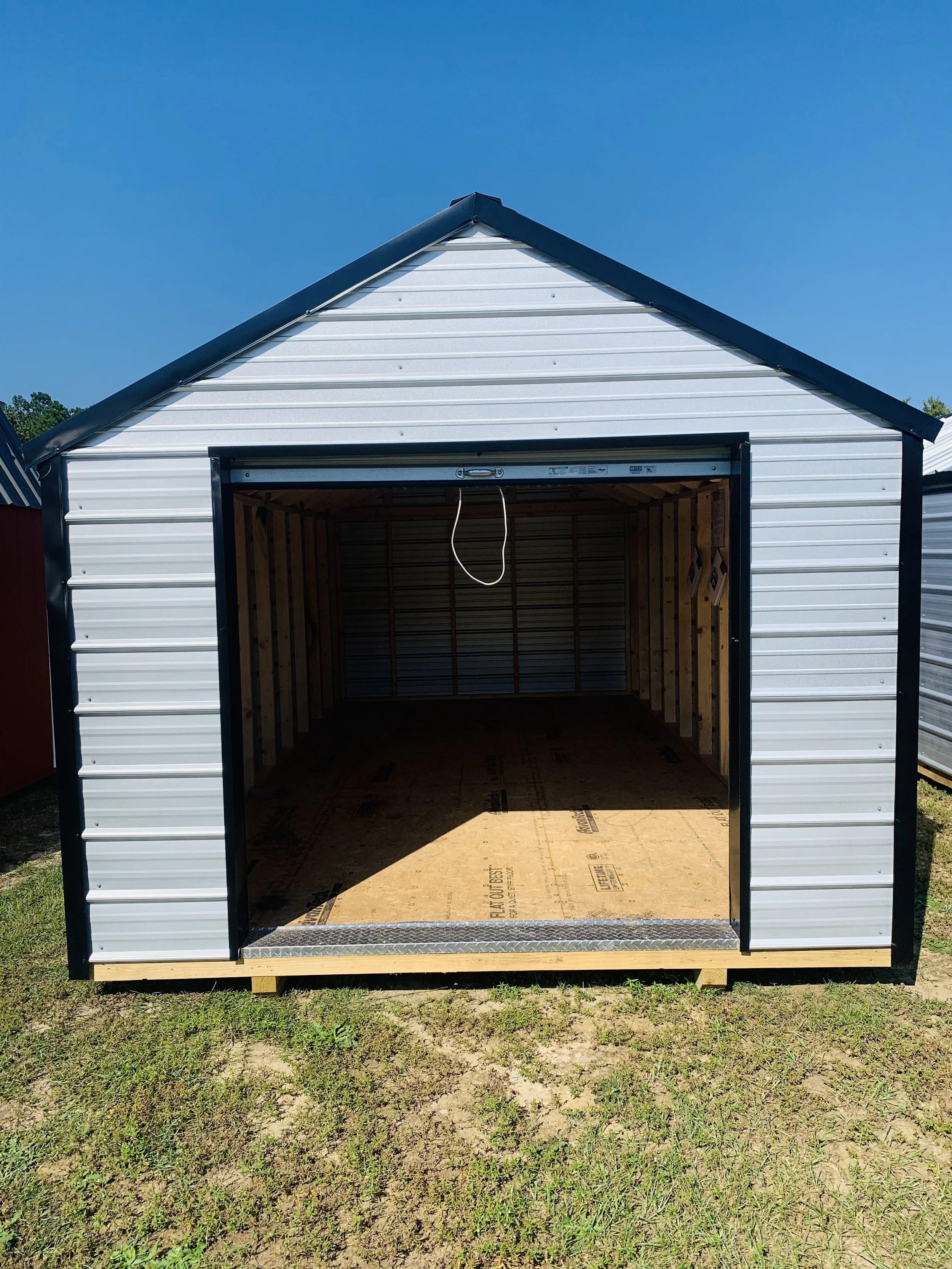 Open shed with metal roof and walls, interior unfinished, on grass.
