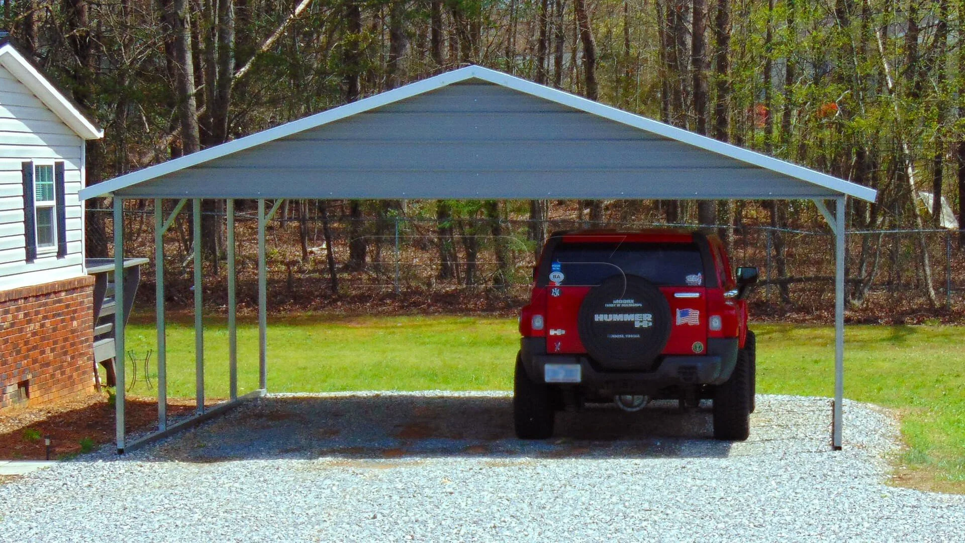 Carport with a red SUV parked underneath on a gravel driveway next to a white house.