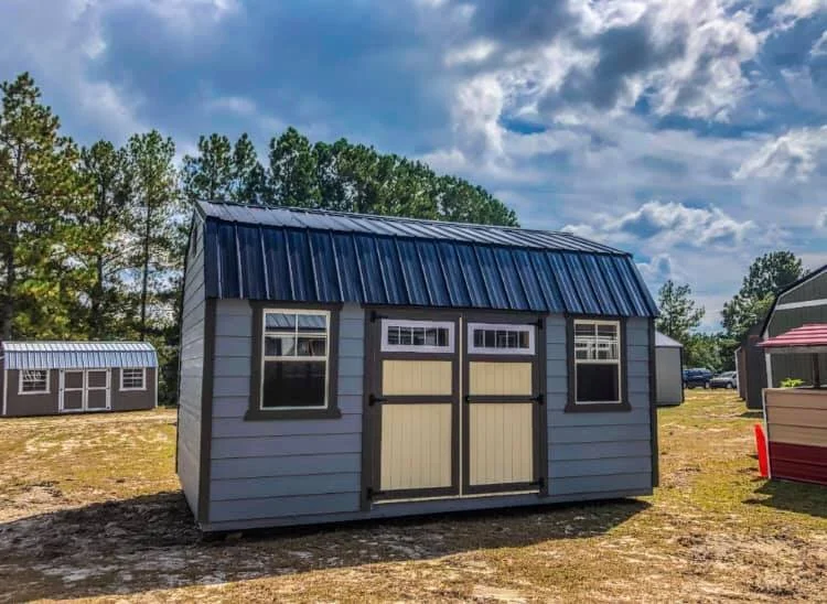 Outdoor storage shed with metal roof and double doors, trees and other sheds in the background.