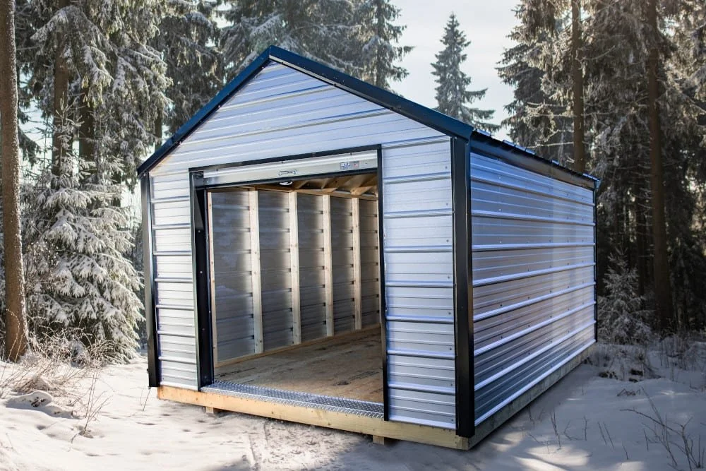Metal shed on snowy ground surrounded by trees
