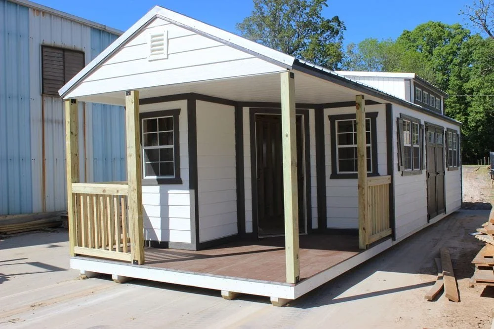 Small white cabin with a porch and multiple windows.