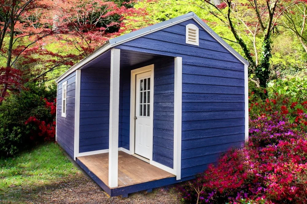 A blue wooden cabin with white trim surrounded by colorful flowering bushes and trees.