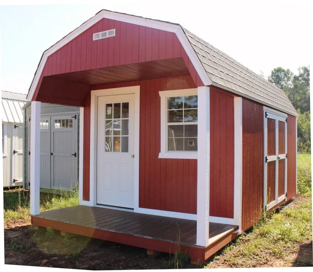 Red and white barn-style shed with a front door, window, and small porch, situated outdoors with trees in the background.