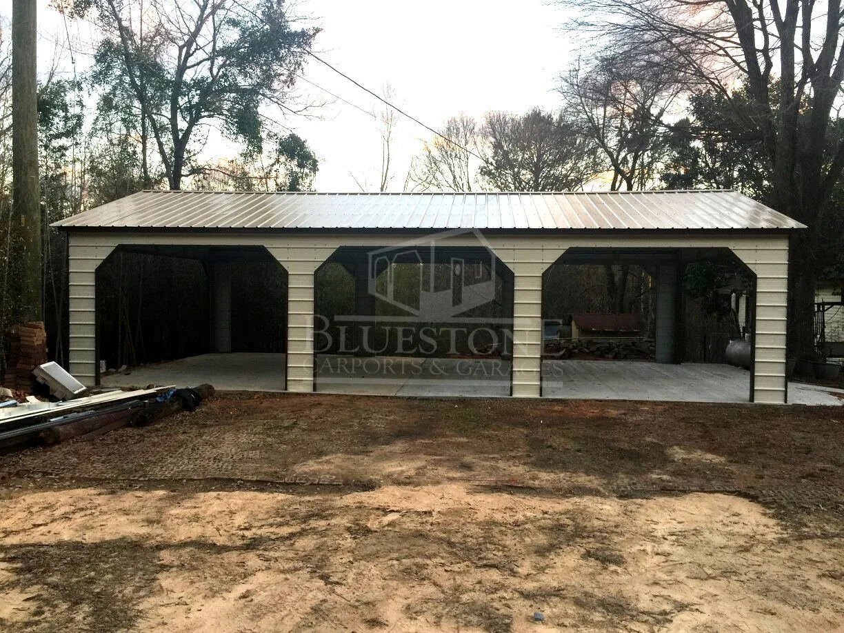 Metal barn with garage and carport surrounded by trees and bare ground.