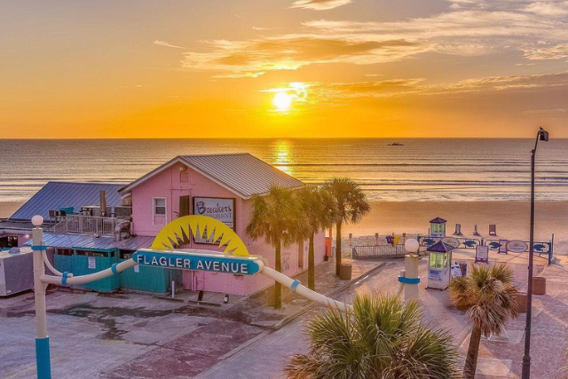 Sunset over the beach with colorful buildings, palm trees, and a playground on the sand.