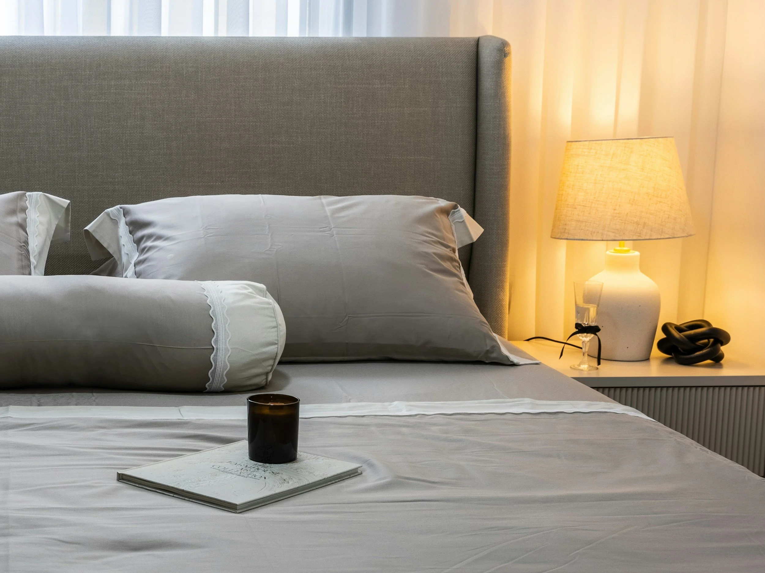 A neatly made bed with light-colored bedding, a bedside lamp, and a closed book creating a peaceful sleep environment — lifestyle and sleep environment design, Nourished by Nicole