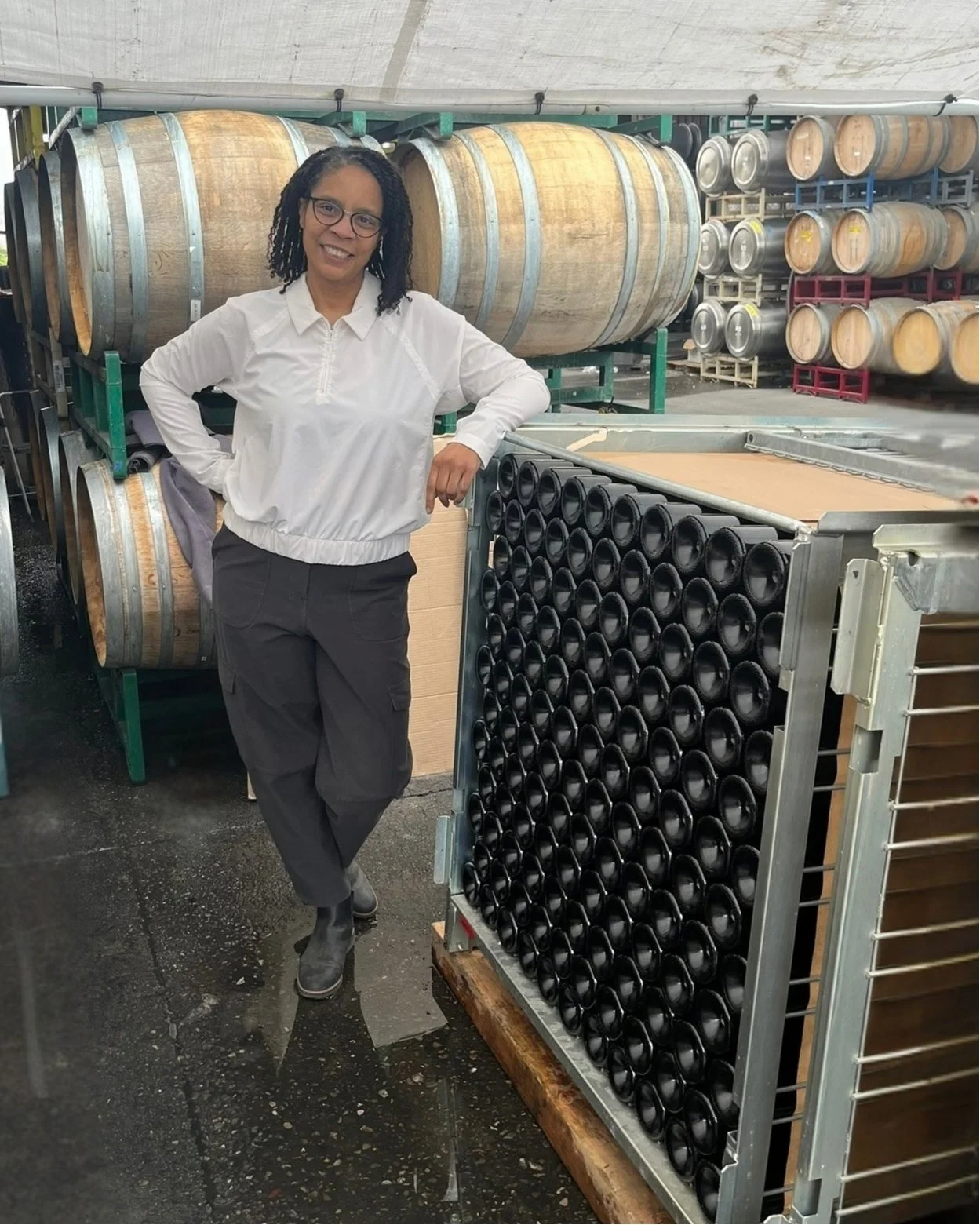 AERILYN founder Tammee Thompson beside a bin of traditional method sparkling wine bottles in tirage, with barrels of base wine behind her.