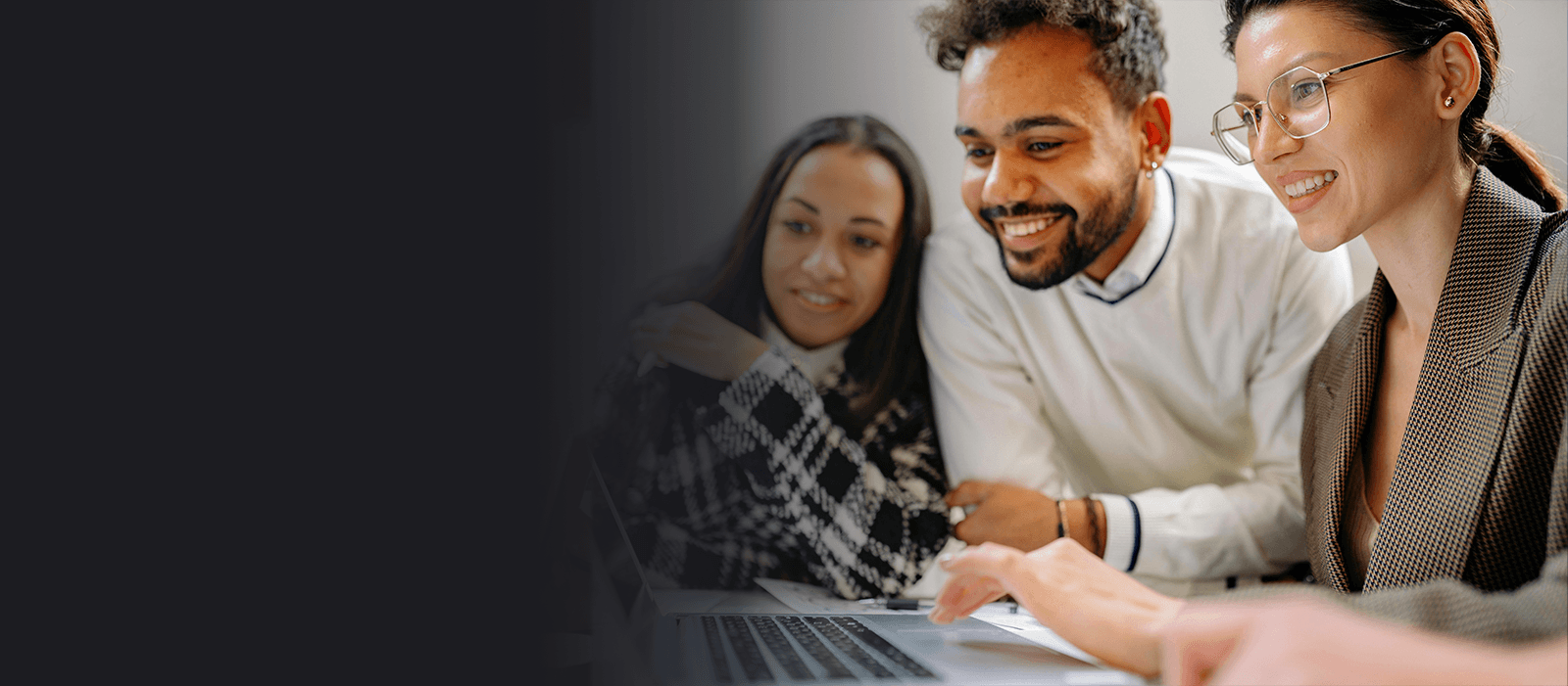 Three diverse adults smiling and looking at a laptop, working together in an office.