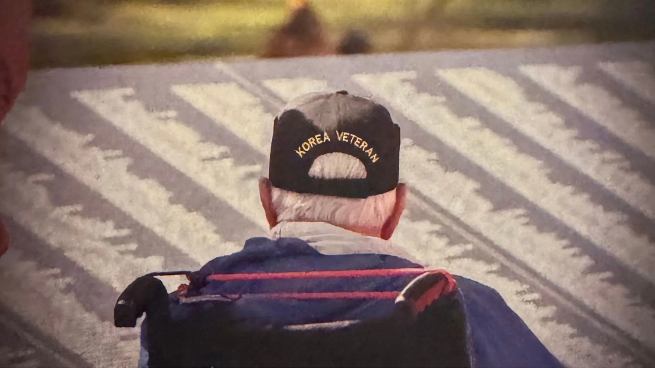 View of a person from behind, wearing a black cap with gold lettering 'KOREA VETERAN,' walking on snow-covered ground at night.