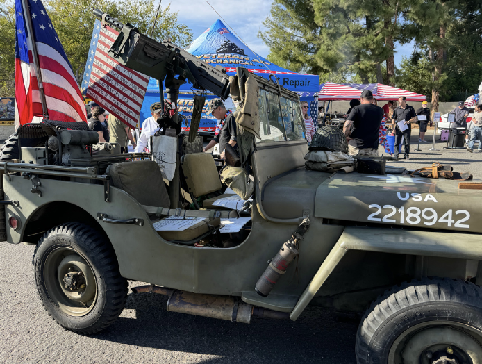 A vintage military Jeep on display at an outdoor event, decorated with American flags and military gear.
