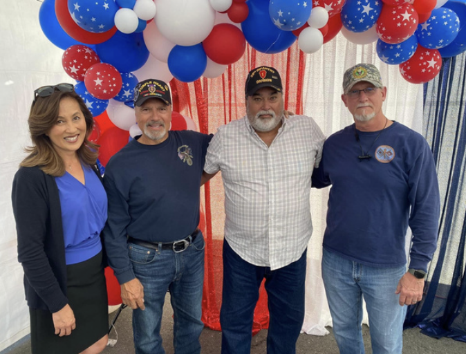 Four people standing in front of patriotic red, white, and blue balloons, smiling at the camera.