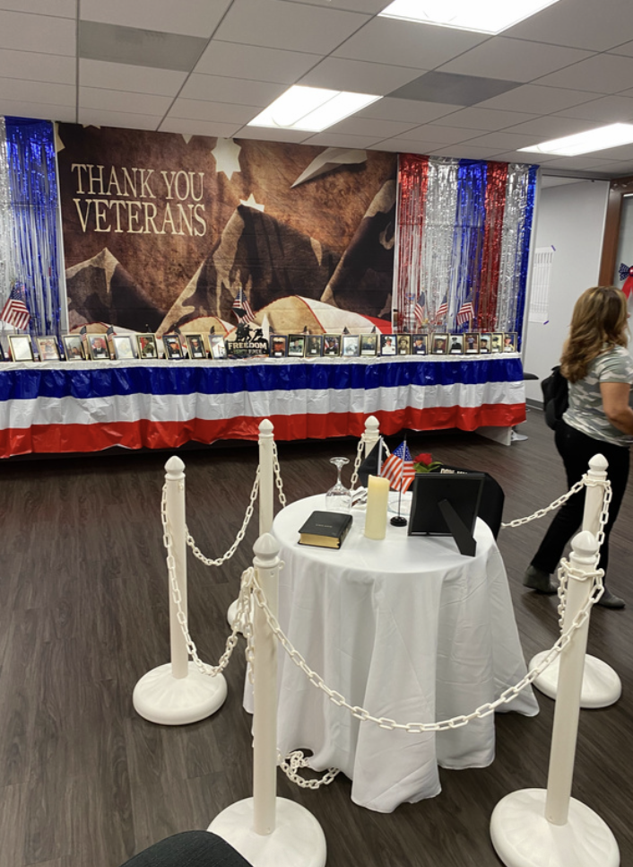 Veterans memorial display with photographs, patriotic decorations, American flags, and a large mural that reads 'Thank You Veterans'.