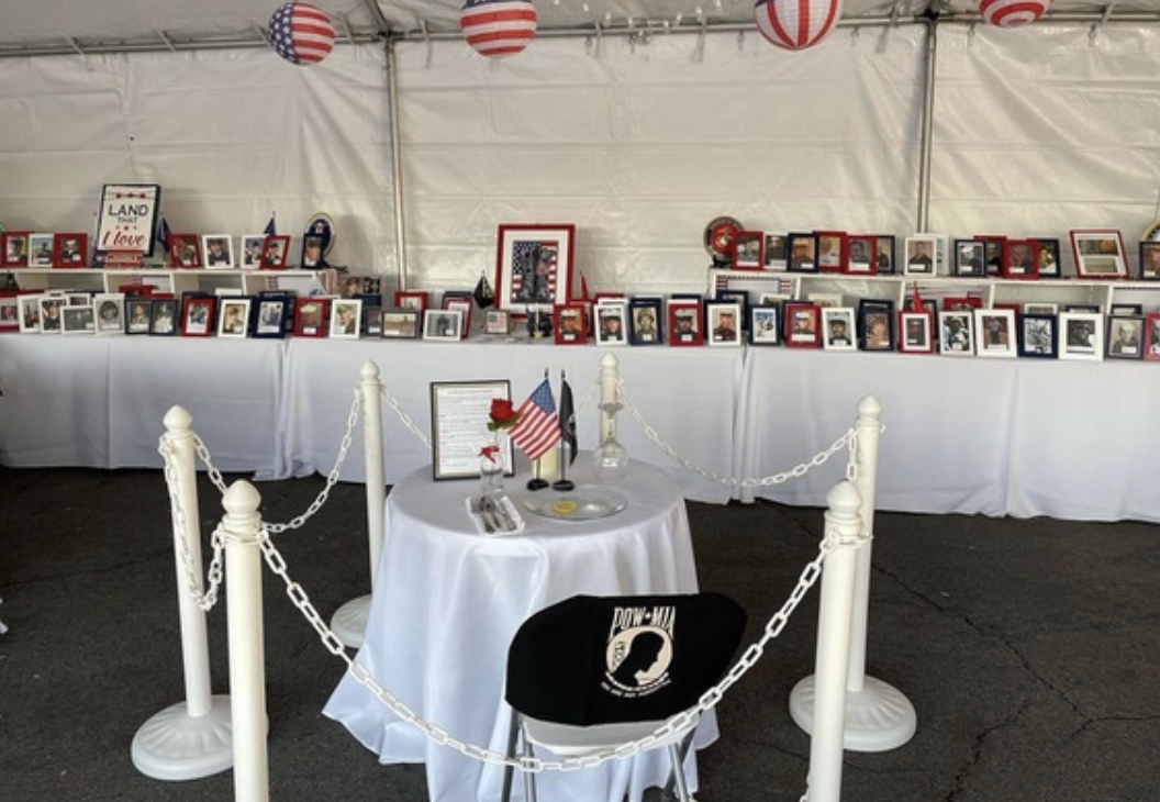 Memorial display with framed photographs of military personnel, American flags, and patriotic decorations inside a white tent.