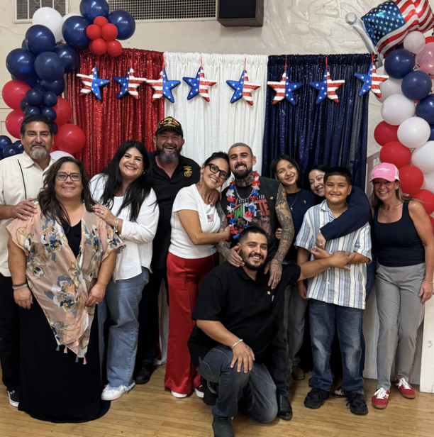 Group of people celebrating an American patriotic event with red, white, and blue decorations, star-shaped balloons, and an American flag-themed backdrop.