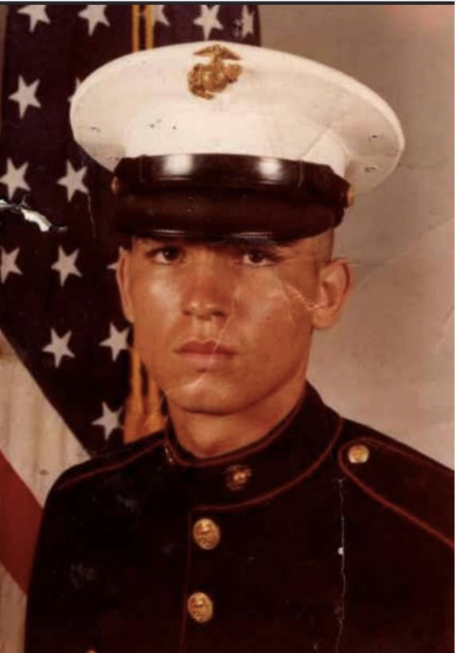 Young man in Marine dress uniform with United States flag in background.