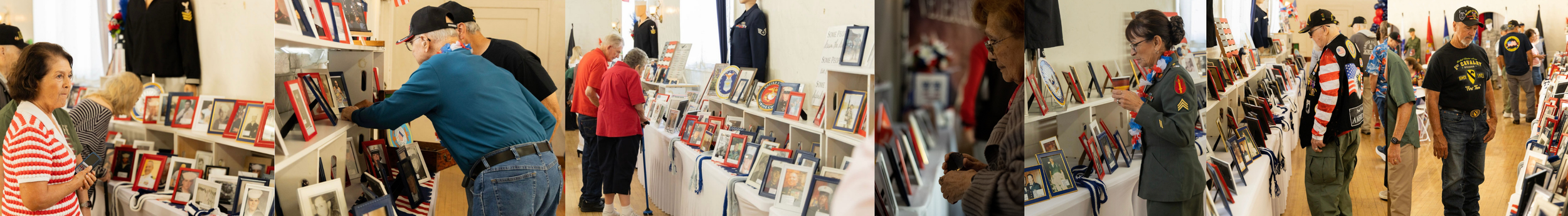 People browsing framed photographs and memorabilia at an indoor event, with some individuals wearing military or veteran jackets.