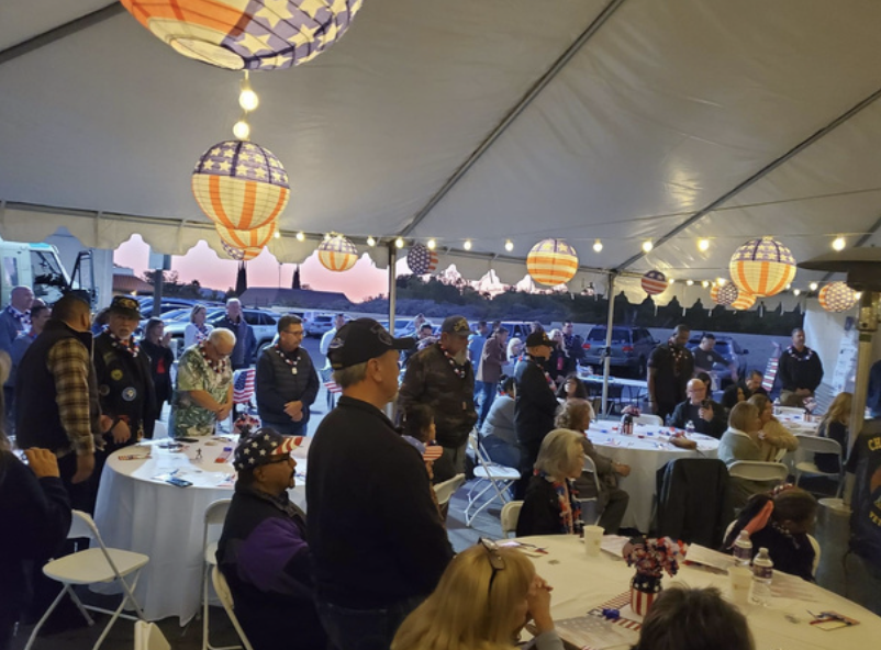 People gathered under a decorated tent with patriotic American-themed lanterns, attending a celebration during sunset.