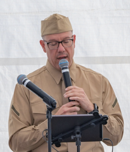 Man dressed as a military soldier speaking into a microphone and reading from a tablet