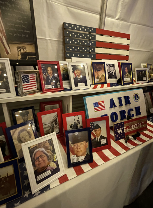 Display of framed photographs of military service members, a wooden American flag artwork, and signs supporting the Air Force. The table is decorated with patriotic red, white, and blue colors.