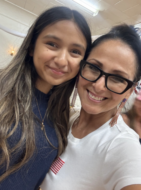 Two women smiling and posing for a selfie indoors, with a ceiling light above.