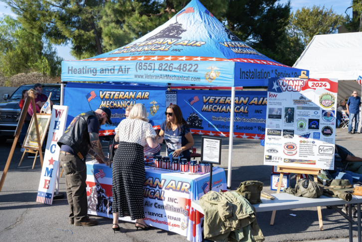 A Veterans Air Mechanical booth at an outdoor event with people talking, patriotic decorations, and informational displays.