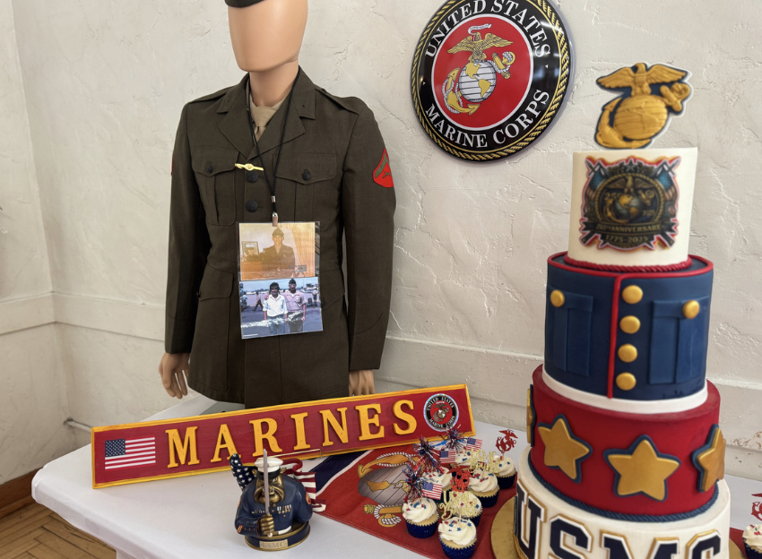 Display of US Marine Corps themed items including a mannequin in uniform, a cake decorated with Marine motifs, a 'Marines' sign, and various patriotic decorations.