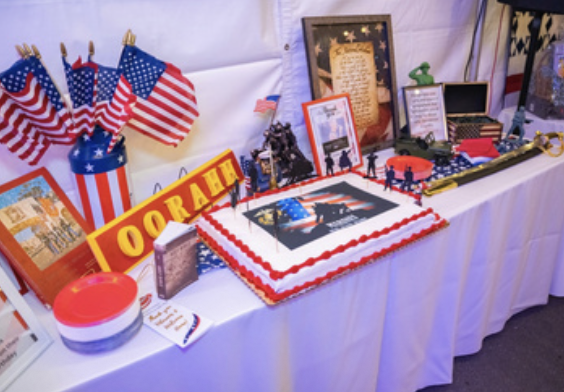 Display table with American flags, a birthday cake with patriotic decorations, and framed photos and signs celebrating the USA.
