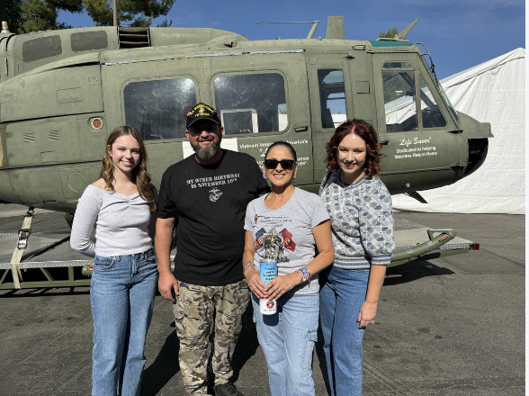 Four people standing in front of a military helicopter at an outdoor event.