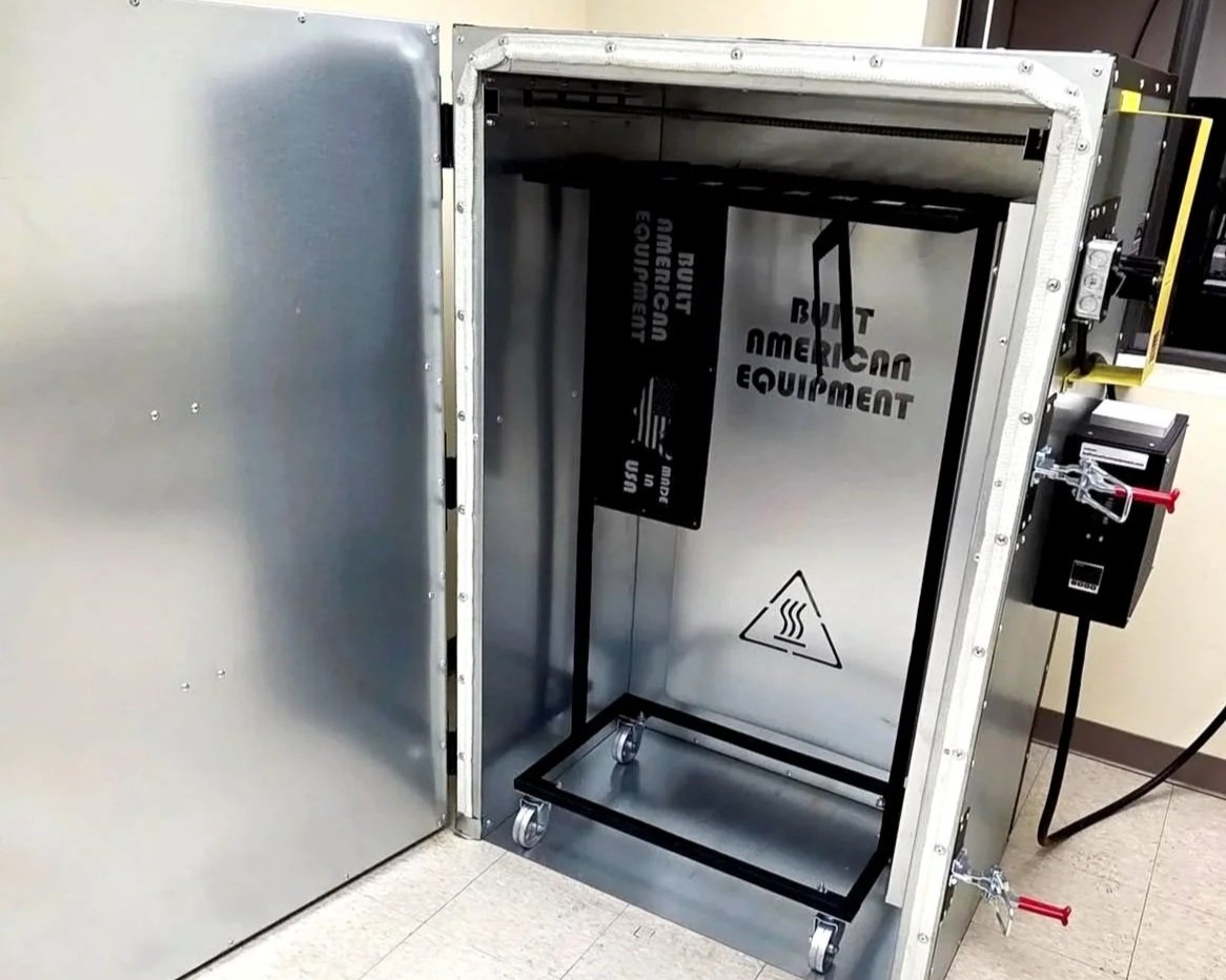 A steel cleanroom with a large, open, rectangular air shower or clean booth with wheels inside.