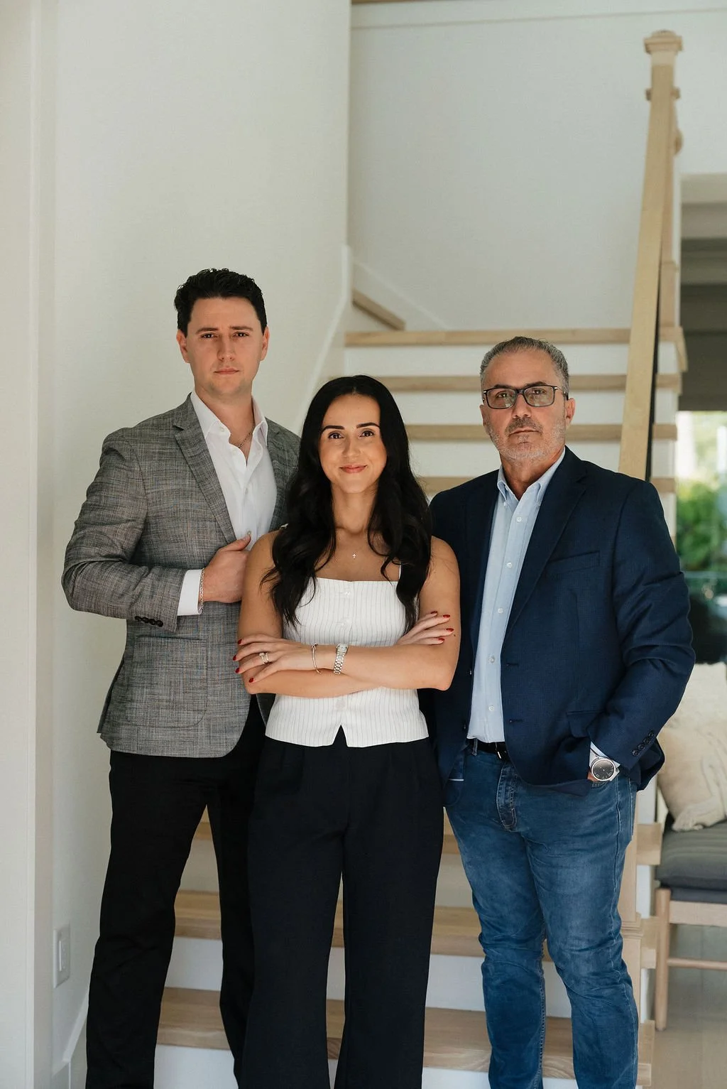 Three professionally dressed individuals standing, with a staircase in the background.