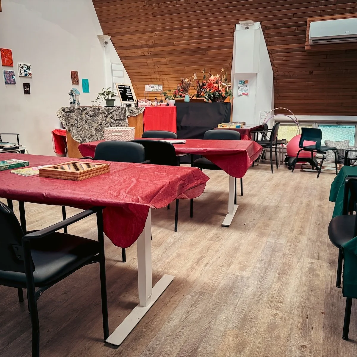 A decorated indoor space with tables covered in red tablecloths, black chairs, and various decorations including flowers, artwork on the wall, and a chessboard on one table.