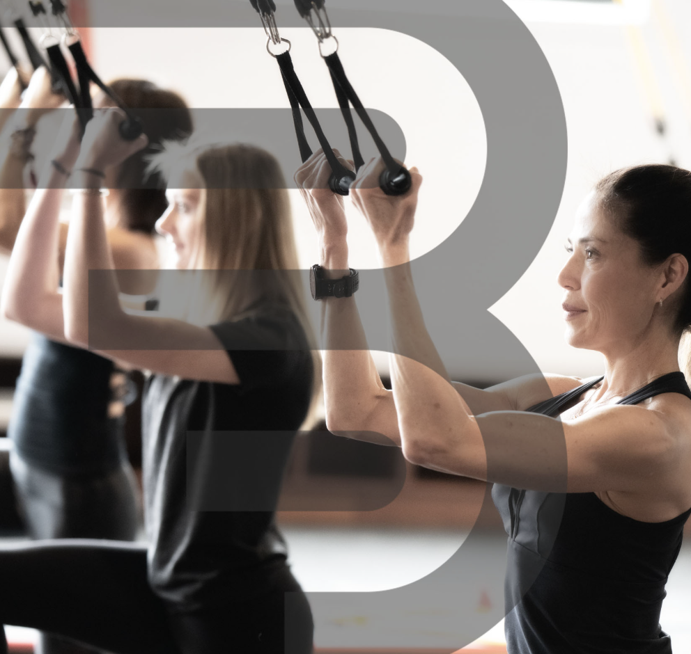Women participating in a fitness class, using suspension training straps, in a gym or fitness studio.