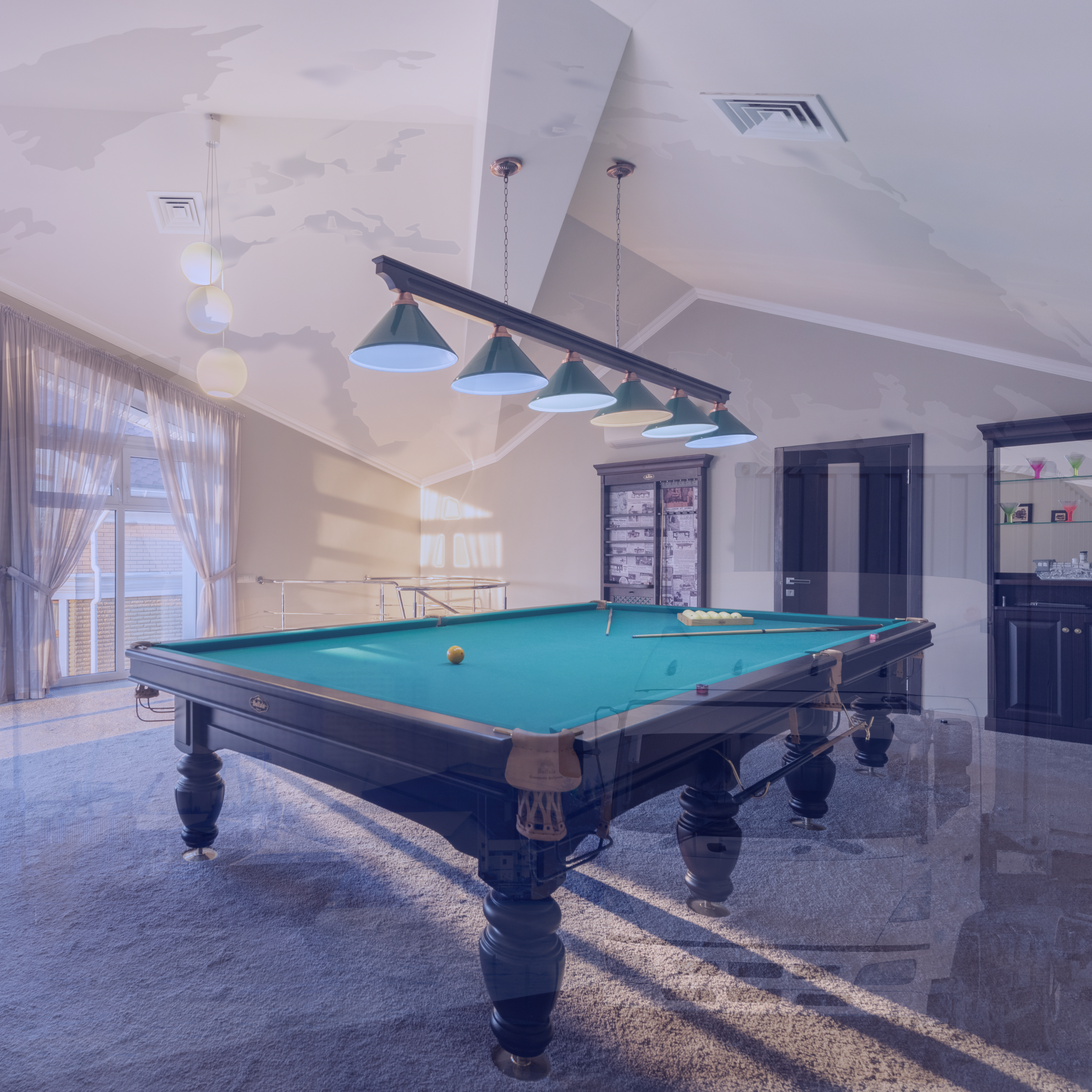 Cozy room with pool table and green lamps, soft lighting, window with sheer curtains, gray carpet, and a bar area in the background.