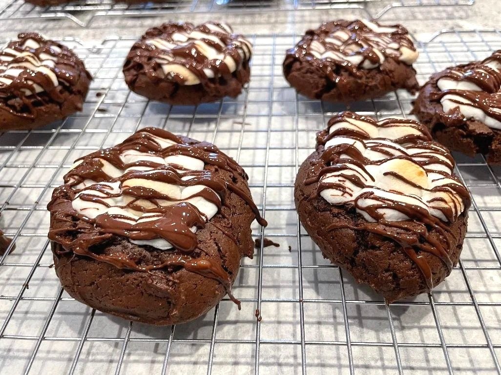 Chocolate cookies topped with white and milk chocolate drizzle cooling on a wire rack.