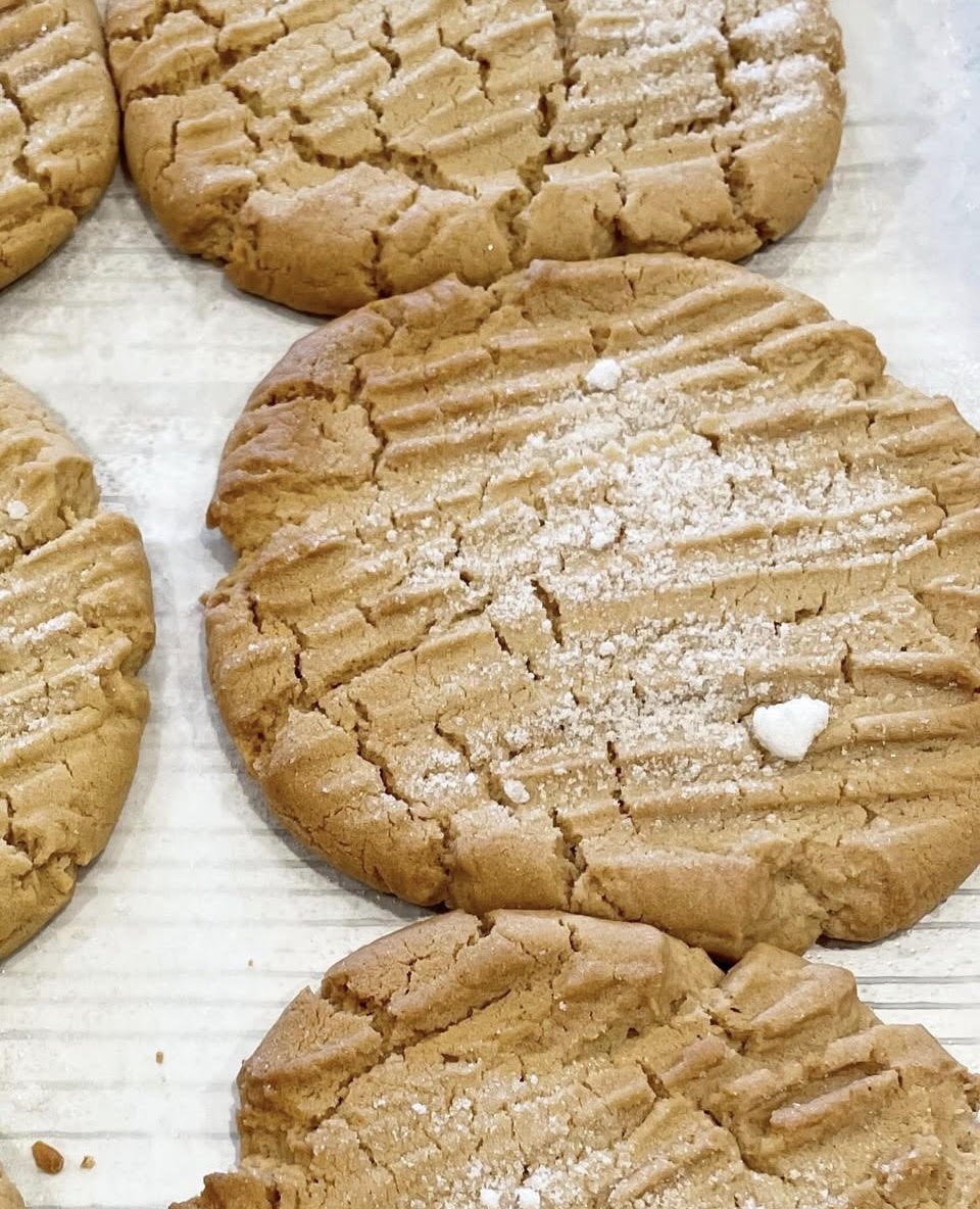 Close-up of several peanut butter cookies sprinkled with sugar on a white surface.